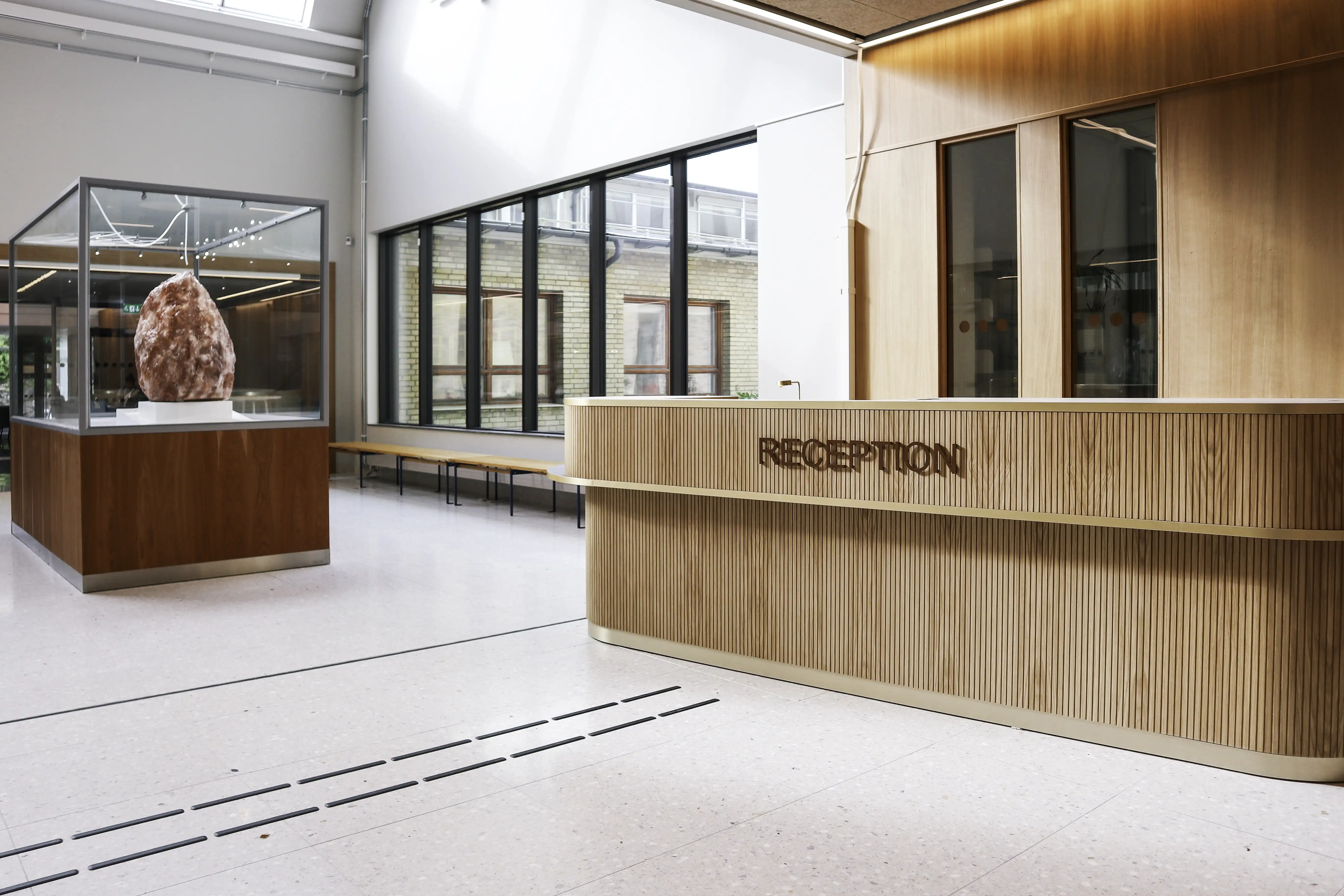 En modern reception med en reception i trä. Lokalen har stora fönster och högt i tak, vilket ger en ljus och öppen atmosfär.