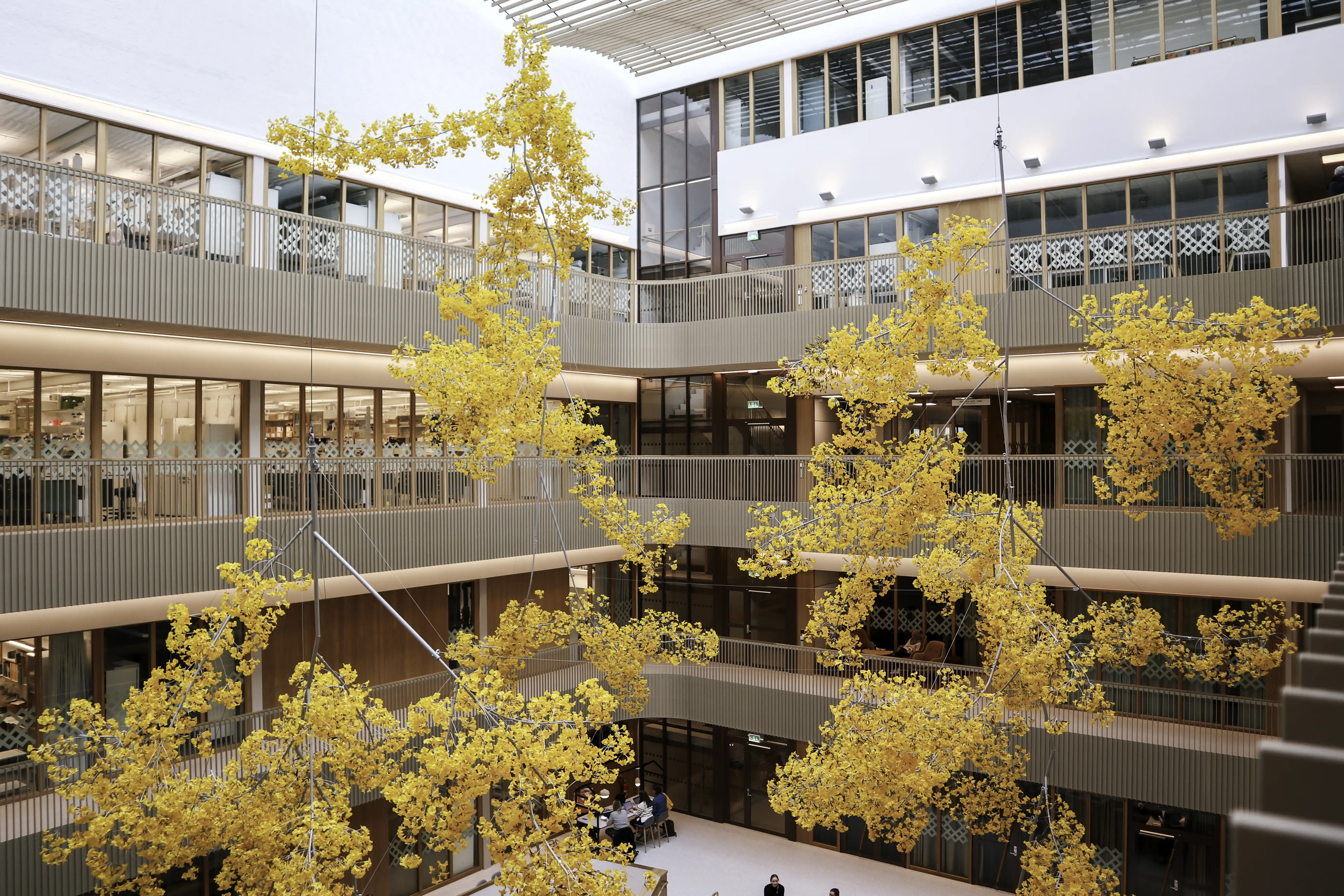 Bilden visar en byggnad i flera våningar med moderna kontorsytor och kontorsmöbler med utsikt över ett öppet centralområde. Designen har glasfönster och balkonger på varje nivå, vilket främjar inspirerande arbetsmiljöer.