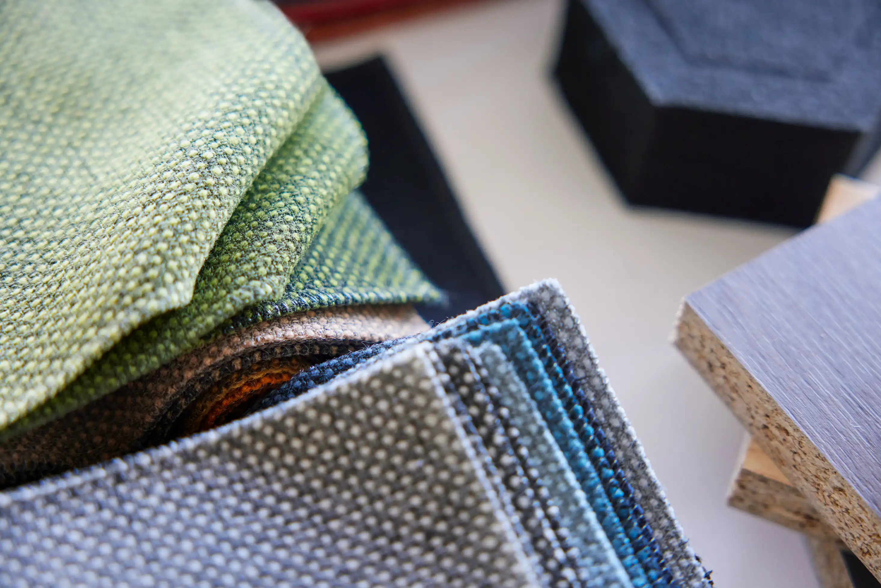 En närbild visar en spridning av tygprover och materialprover i olika texturer och färger. Vissa trämaterial och prover syns också i bakgrunden.