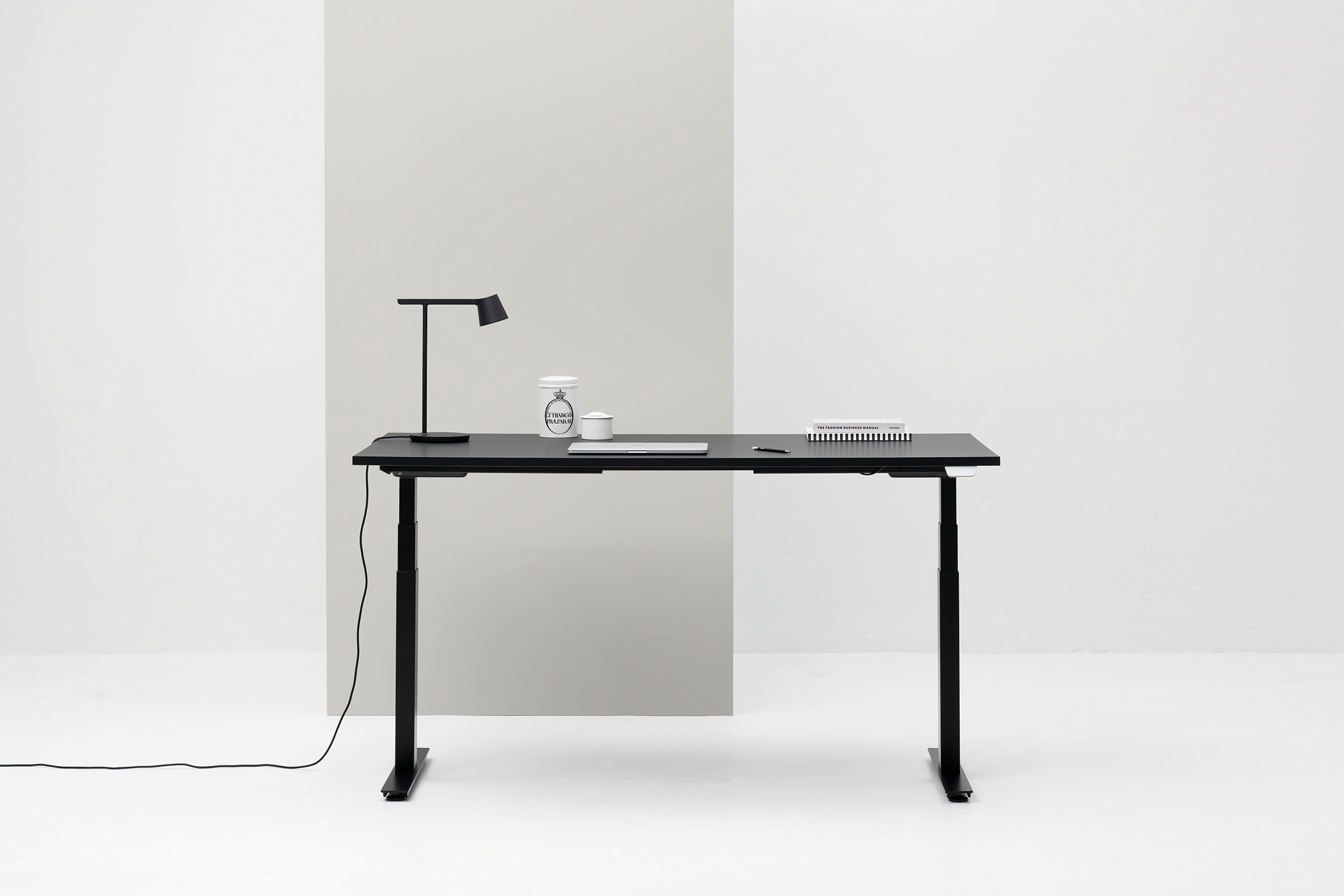 Ett minimalistiskt svart skrivbord. Bakgrunden är vit med en ljusgrå panel. Skrivbordet i bilden har en modern design.
